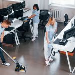 Cleans floor. Group of workers clean modern office together at daytime.