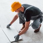 Installation of plate. Man in grey uniform and orange hard hat works indoors in modern big office at daytime.