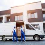 Two removal company workers unloading boxes from minibus into new home.