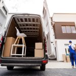 Two removal company workers unloading boxes and furniture from minibus.